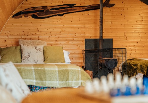 cosy rounded roof cabin, fully wooden throughout with A log burning stove sitting beside the double bed, Olive green textiles and natural furs decorate the glamping accommodation.